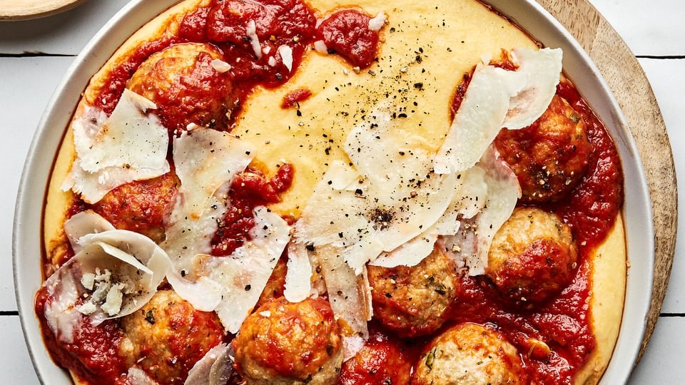 homemade chicken meatballs with polenta topped with shaved parmesan and marinara in a bowl with a spoon