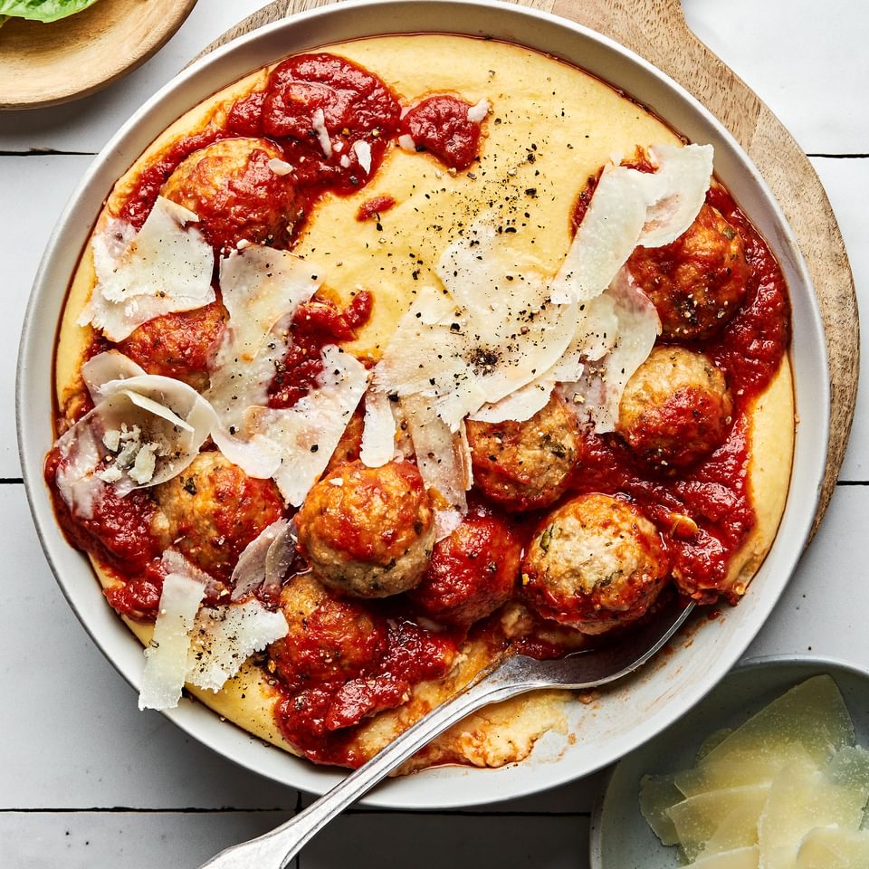 homemade chicken meatballs with polenta topped with shaved parmesan and marinara in a bowl with a spoon