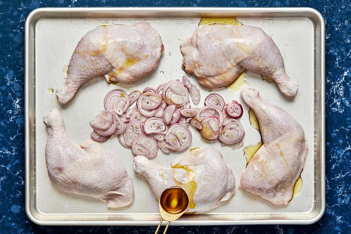 chicken quarters patted dry, seasoned with salt and sliced shallots on a baking sheet ready for the oven
