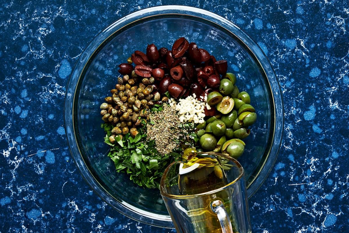 olives, capers, parsley, garlic, Italian seasoning, red wine vinegar, olive oil, salt & pepper being tossed in a bowl