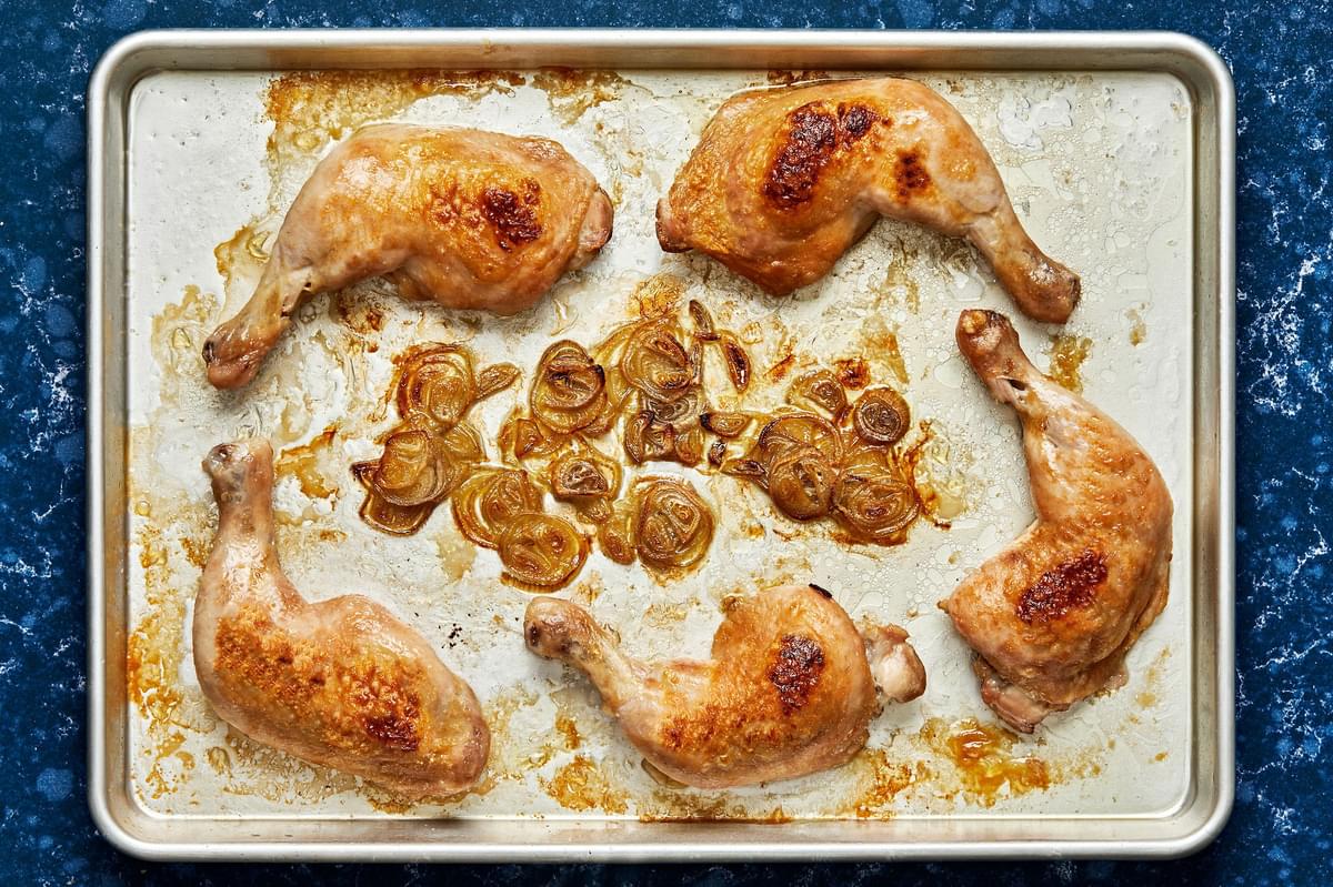 Chicken Quarters and shallots seasoned with salt that have been baked in the oven on a baking sheet
