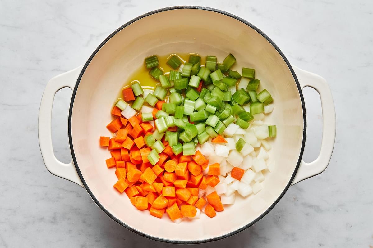 chopped onion, carrots, and celery being cooked in olive oil in a stock pot