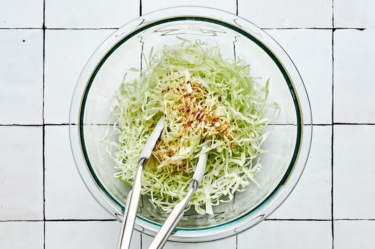 seasoned cabbage being tossed with tongs made with shredded cabbage, salt, pepper, taco seasoning, white vinegar & olive oil