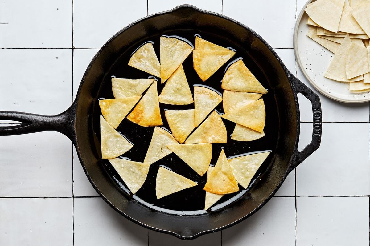 homemade corn tortilla chips being fried in vegetable oil in a skillet