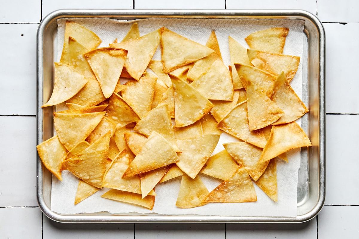 homemade tortilla chips sprinkled with salt cooling on a parchment lined baking sheet