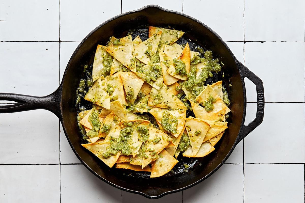 homemade tortilla chips in a frying pan drizzled with salsa verde to make chilaquiles