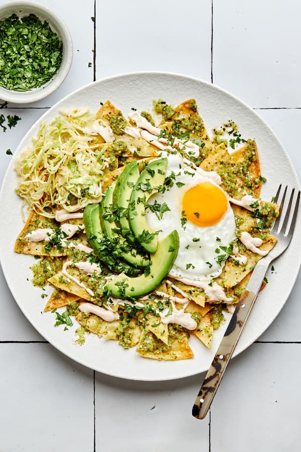 chilaquiles on a plate made with homemade tortilla chips topped with cabbage, salsa verde, crema, avocado and a fried egg