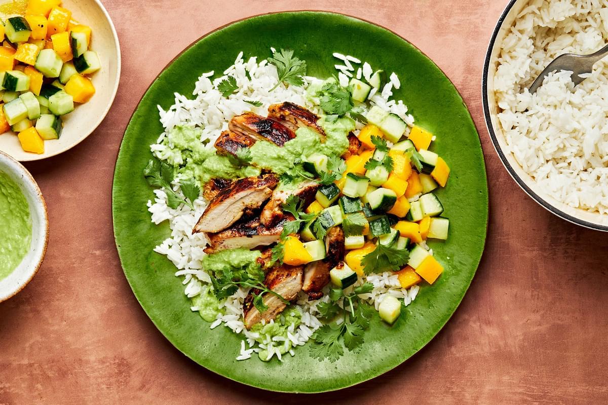 A Citrus Chicken Rice Bowl with Ginger Jalapeño Sauce beside bowls of additional coconut rice, sauce and cucumber salad