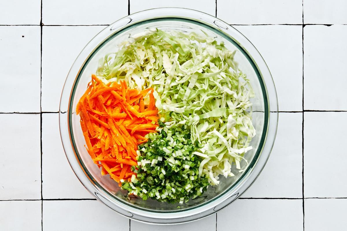shredded cabbage, shredded carrots and minced green onions in a glass bowl to make classic coleslaw
