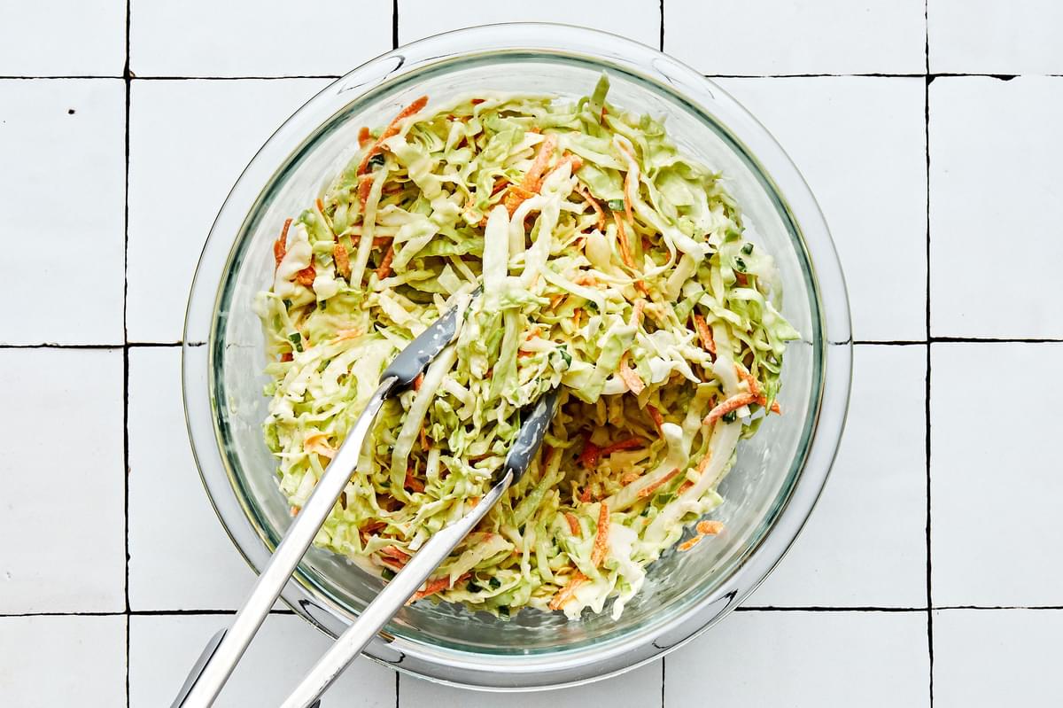 shredded cabbage, shredded carrots and minced green onions being tossed with dressing to make classic coleslaw