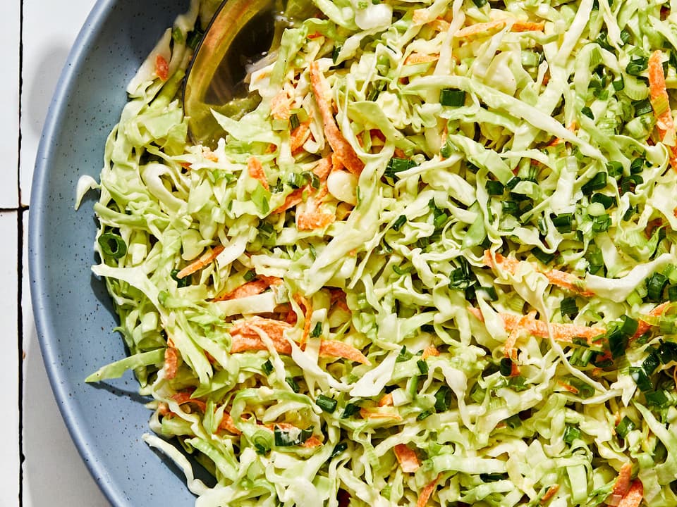 homemade classic coleslaw in a serving bowl with a wooden serving spoon on the counter