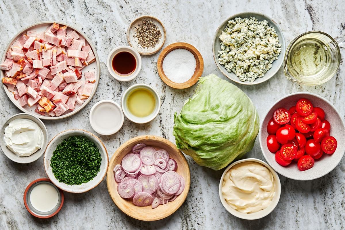 bacon, iceberg lettuce, shallots, cherry tomatoes, blue cheese crumbles & other ingredients in bowls for classic wedge salads