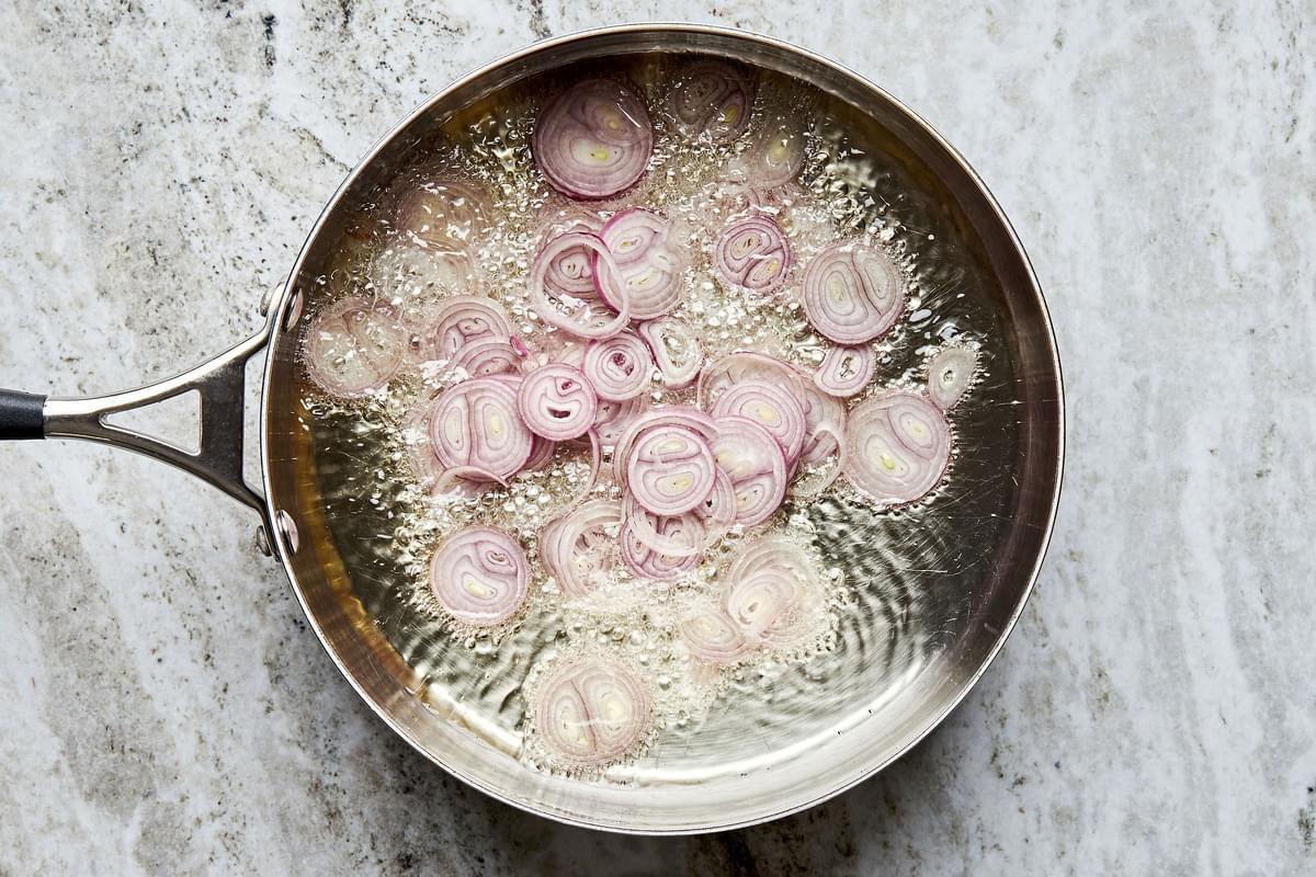 thinly sliced shallots being fried in vegetable oil in a pan