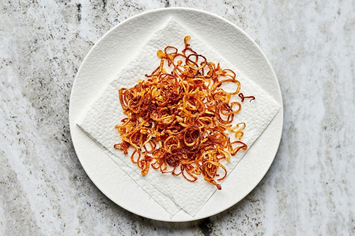 thinly sliced fried shallots on a a paper towel lined plate