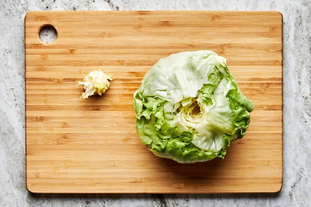 a whole head of iceberg lettuce on top of a wooden cutting board