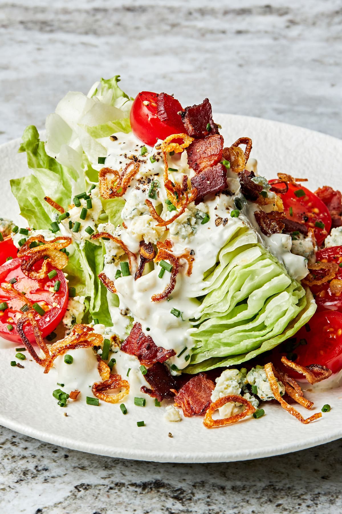 a classic wedge salad topped with homemade blue cheese dressing, blue cheese, bacon, cherry tomatoes and fried shallots