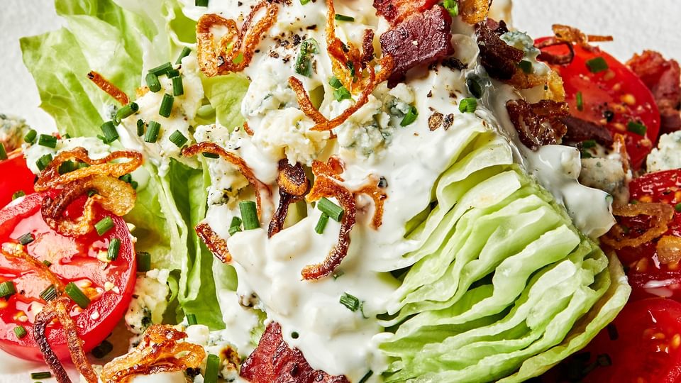 a classic wedge salad topped with homemade blue cheese dressing, blue cheese, bacon, cherry tomatoes and fried shallots