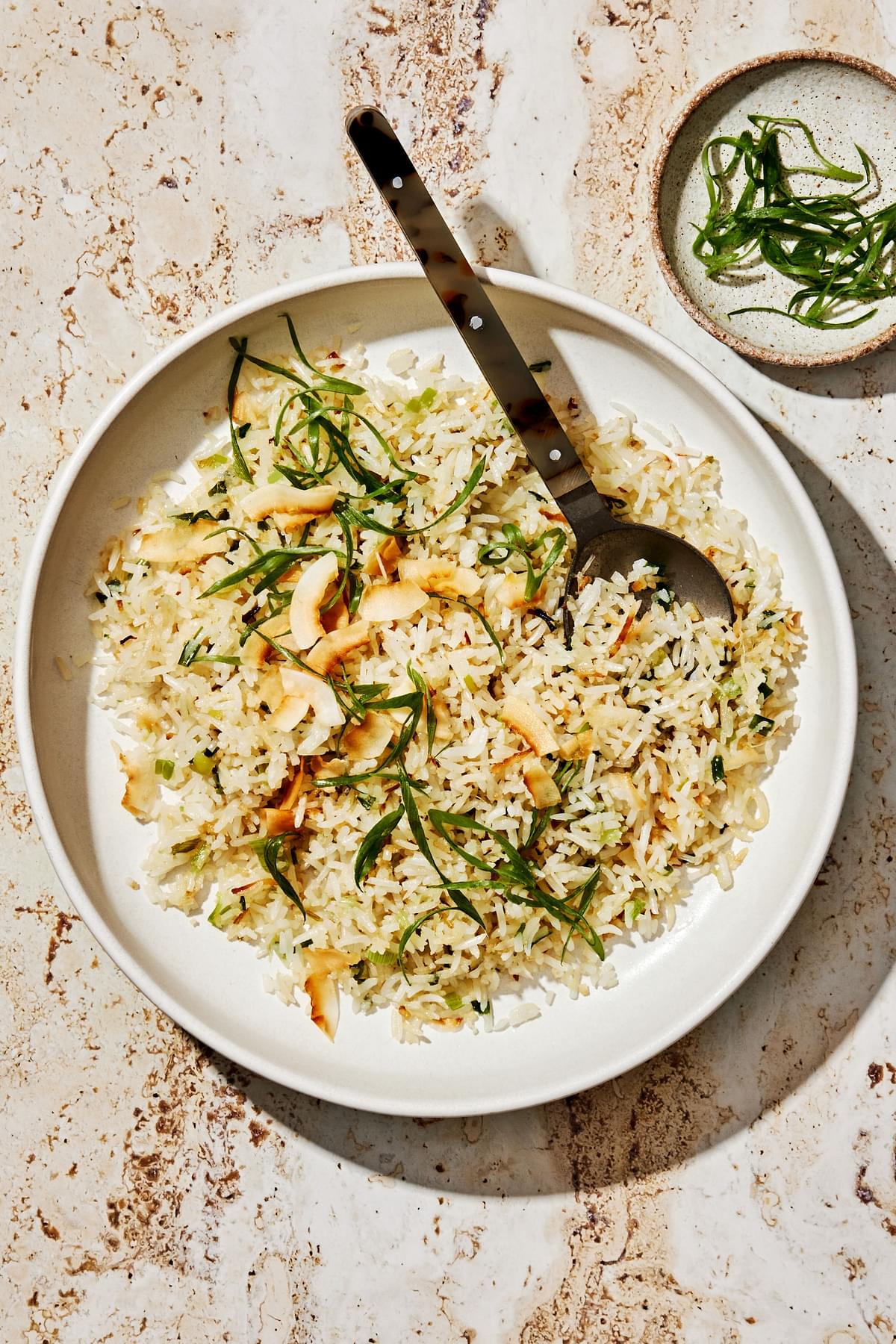 homemade coconut fried rice with green onions, ginger, and sweetened coconut flakes in a serving bowl with a wooden spoon