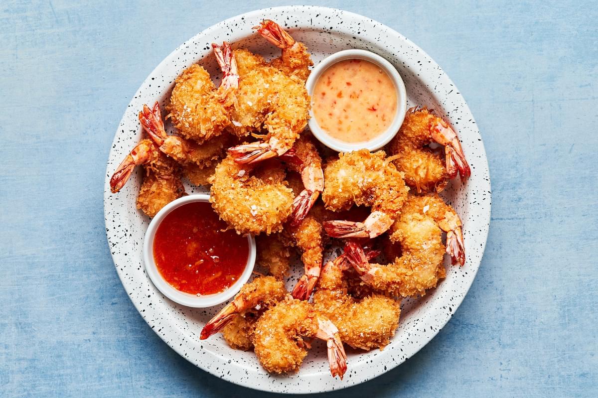 homemade coconut shrimp on a serving platter with 2 bowls of homemade curry sauce and ginger mayo for dipping