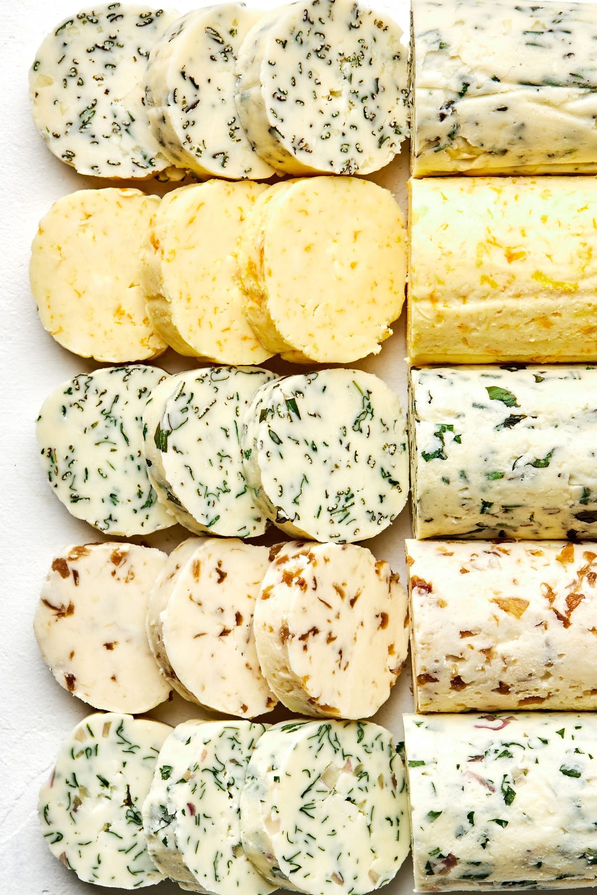 5 sticks of compound butters lined up and sliced made with fresh herbs, citrus zest and juice and caramelized onions