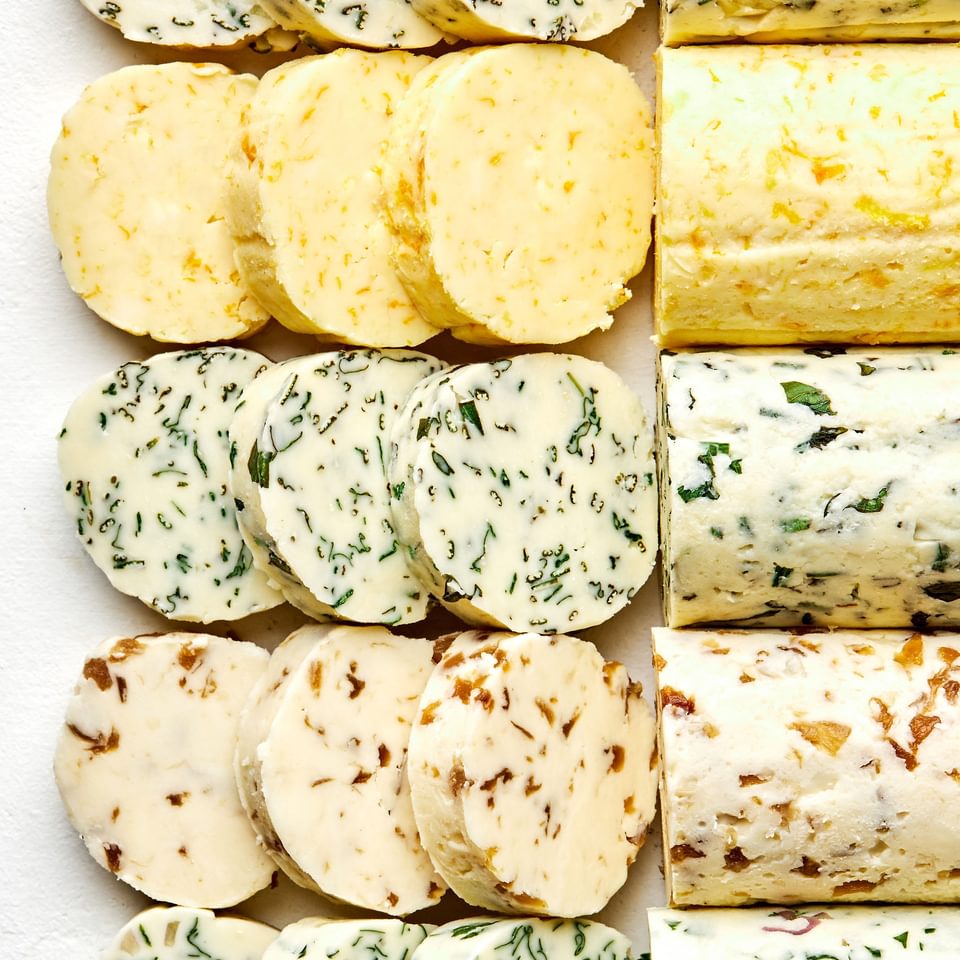 5 sticks of compound butters lined up and sliced made with fresh herbs, citrus zest and juice and caramelized onions