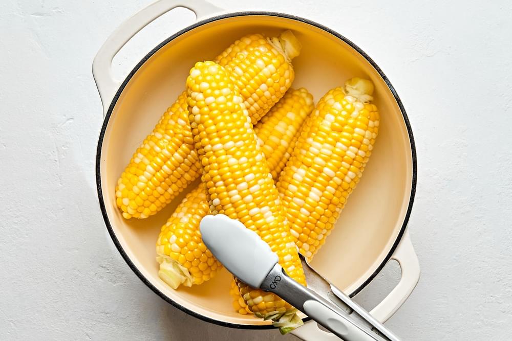 corn on the cob cooked in a pot of boiling water being removed with tongs to transfer to a serving platter