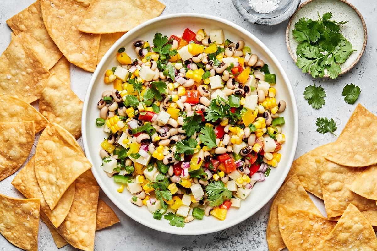 homemade cowboy caviar in a serving bowl surrounded by tortilla chips and bowls of salt and cilantro