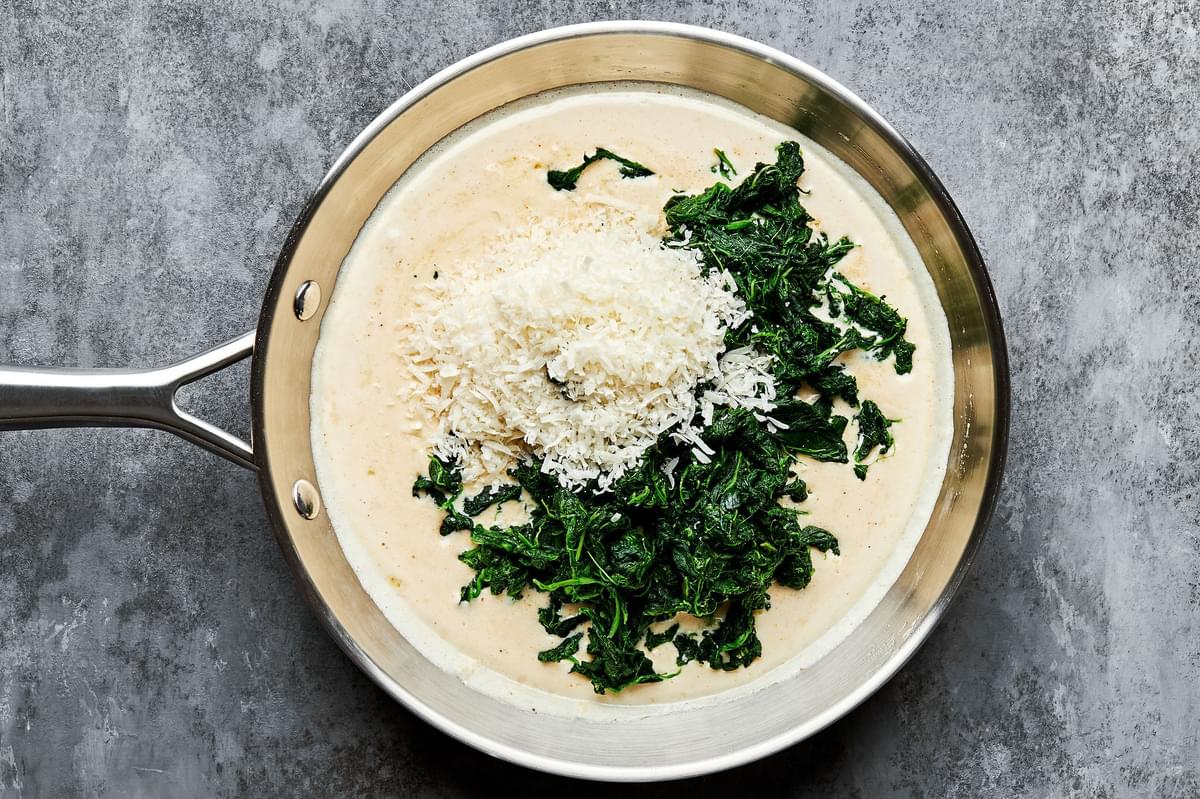 spinach and parmesan being added in a skillet with cream shallot, butter, garlic, dijon and spices to make creamed spinach