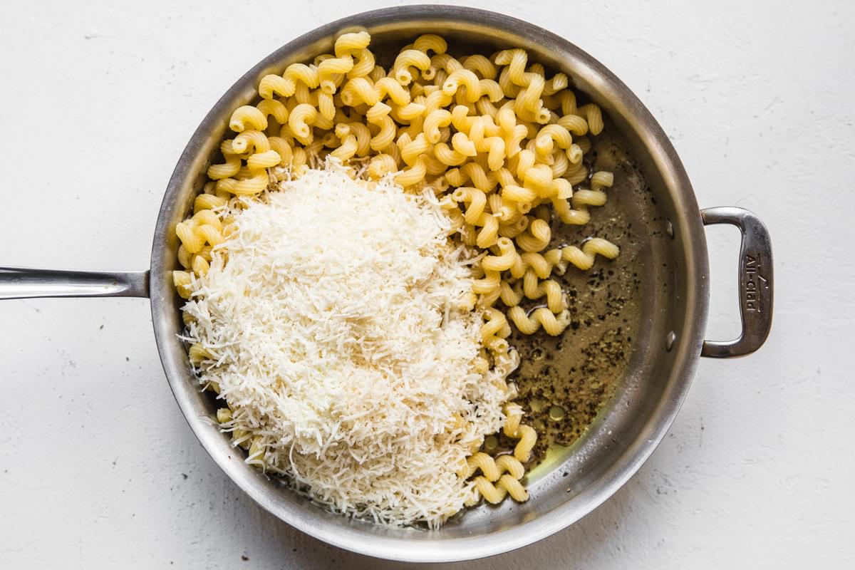 cooked cavatappi and finely grated Parmigiano-Reggiano being stirred into olive oil and cracked pepper in a large skillet