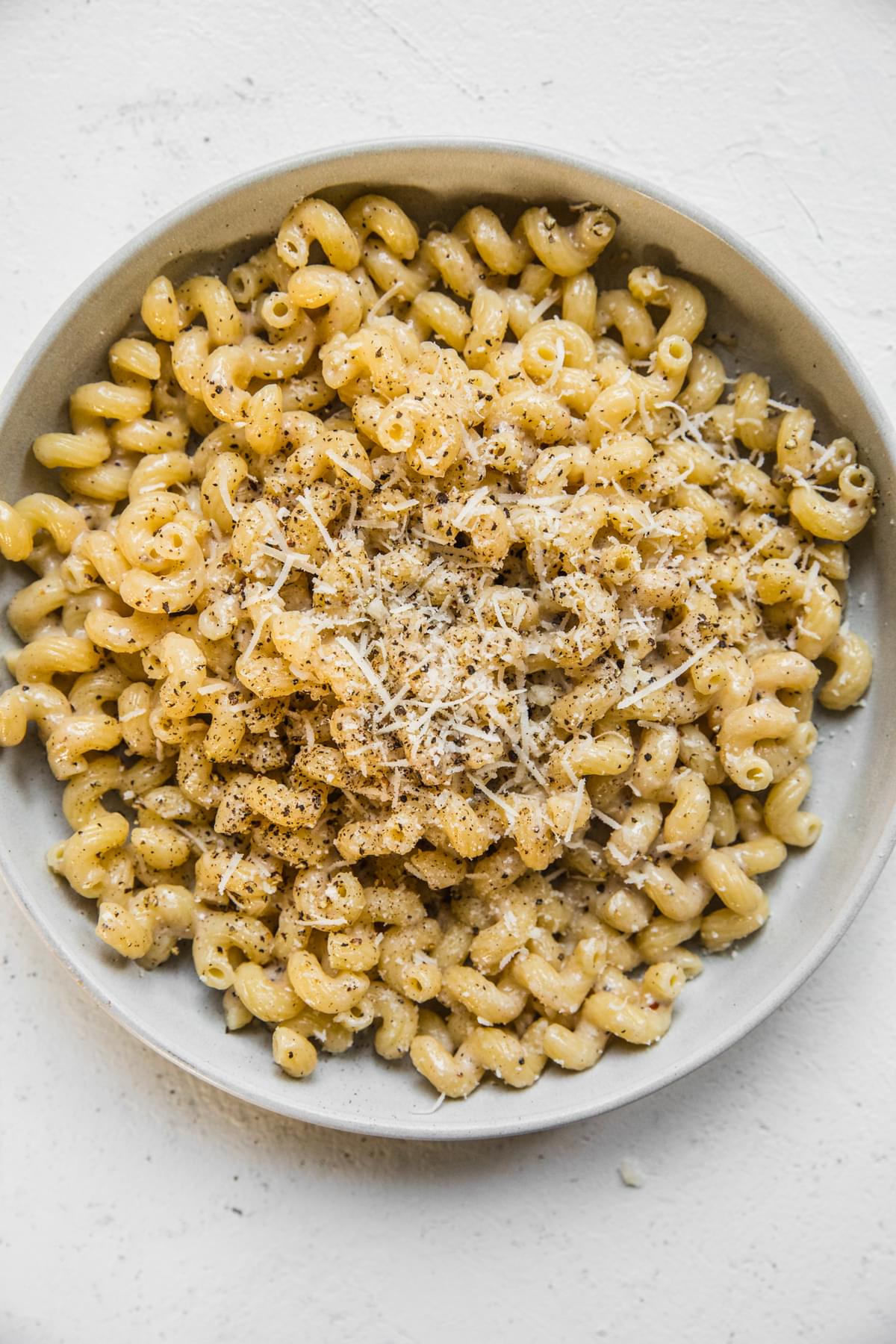homemade Creamy Cavatappi in a bowl topped with grated Romano and parmigiano and coarsely cracked pepper
