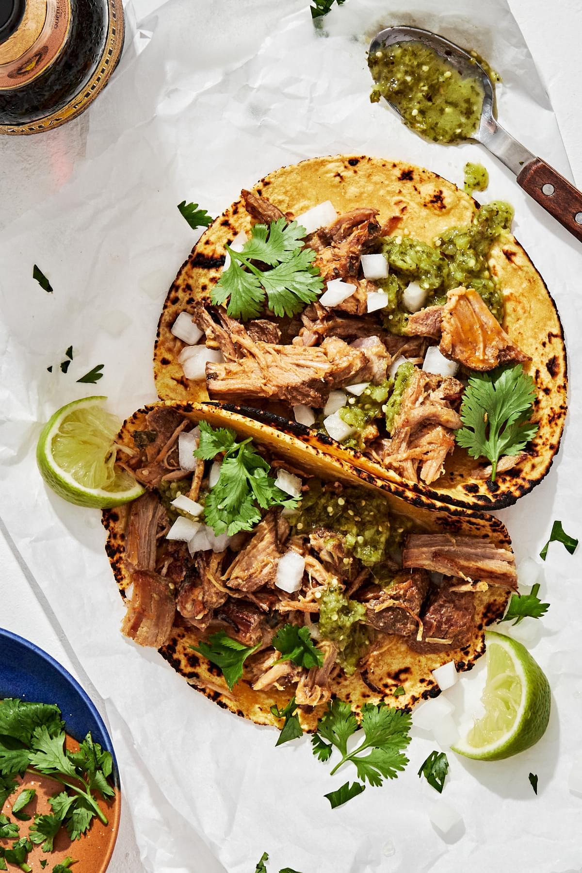 crispy carnitas tacos in homemade corn tortillas topped with onion, cilantro and salsa verde served with lime wedges