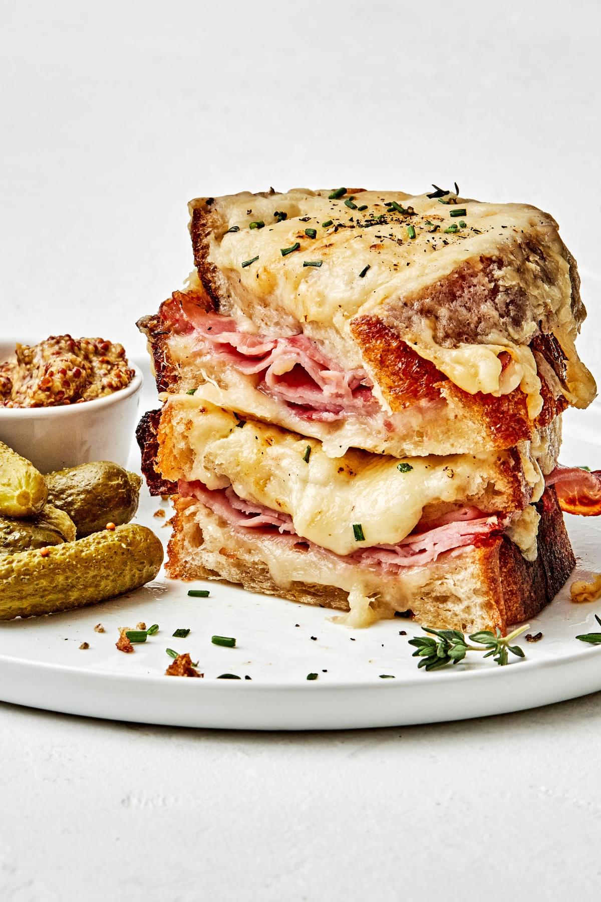 a homemade croque monsieur sandwich stacked on a plate served with pickles and stone ground mustard