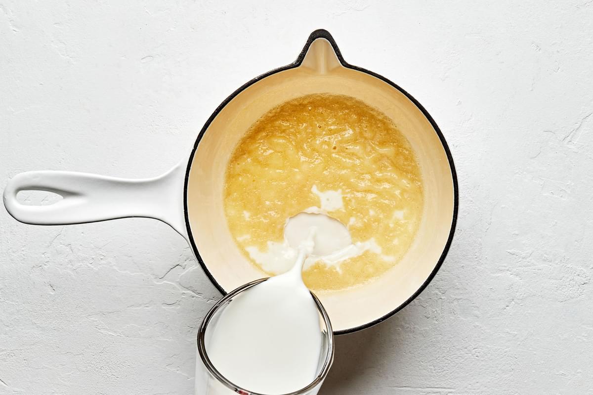 milk being poured into a pot with melted butter to make a béchamel sauce