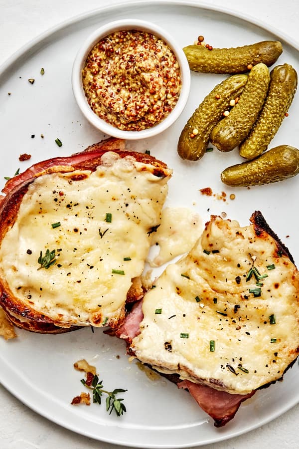 a homemade croque monsieur sandwich on a plate served with pickles and stone ground mustard