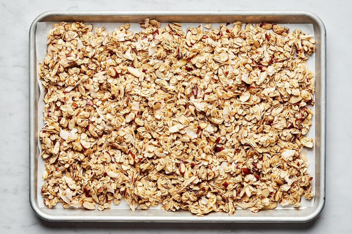 granola made with oats, sliced almonds, salt, brown sugar, maple syrup, oil and vanilla on a baking sheet