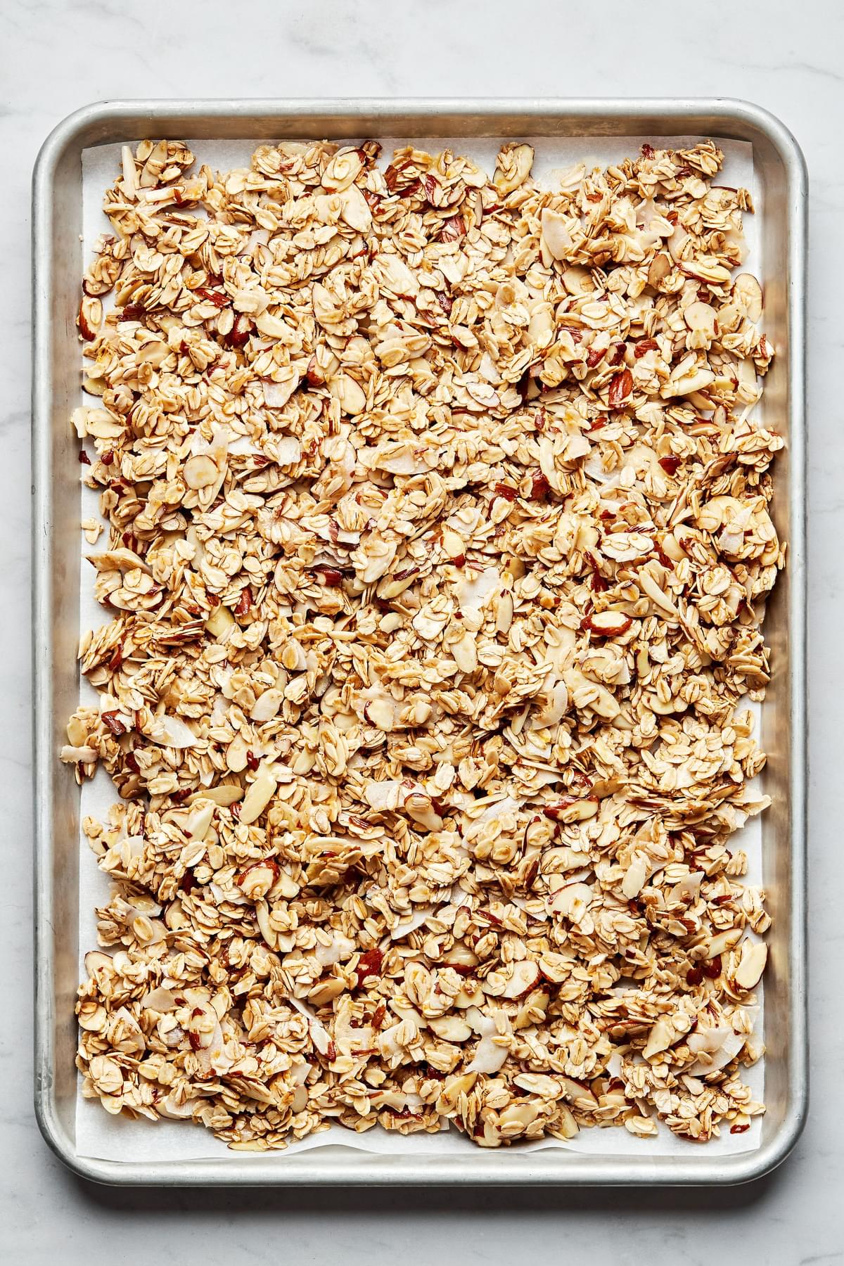 easy homemade granola baked in the oven on a parchment lined baking sheet made with oats, almonds, brown sugar and maple