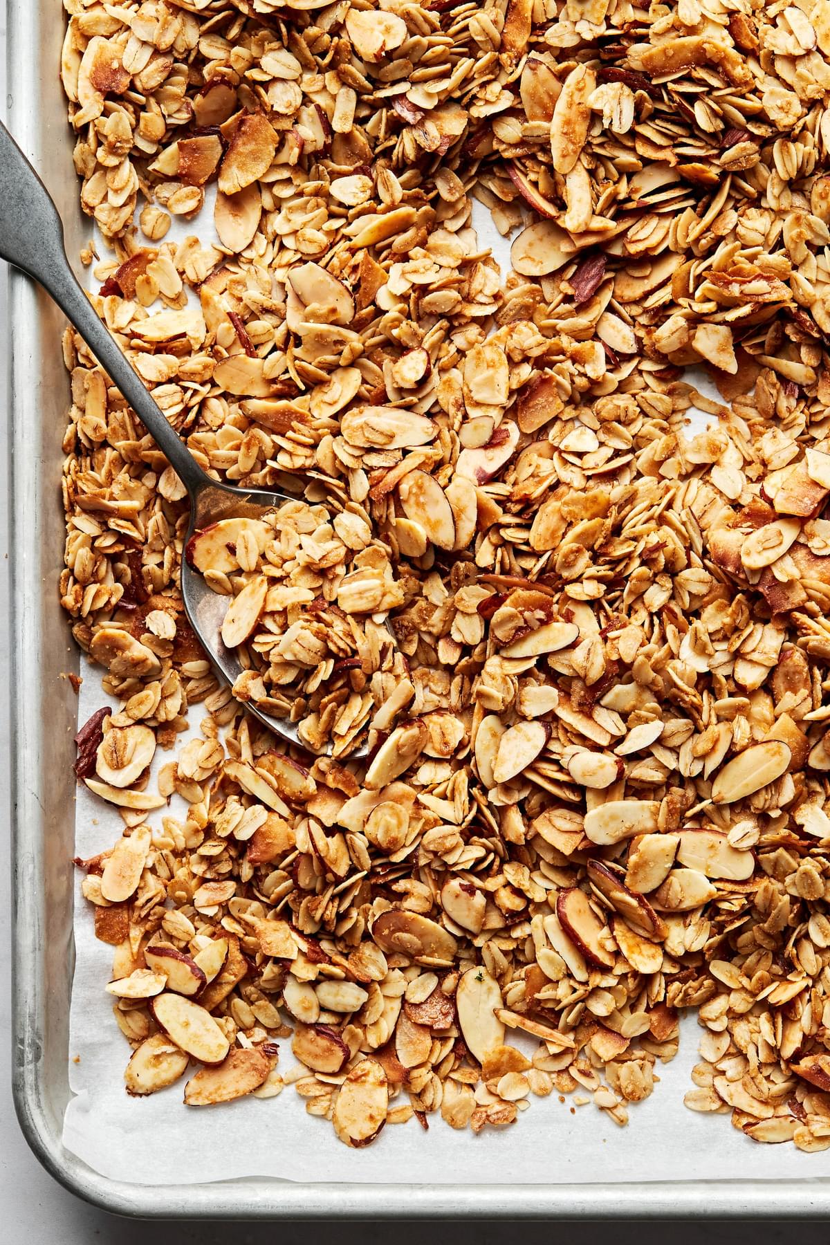easy homemade granola on a parchment lined baking sheet being stirred with a spoon