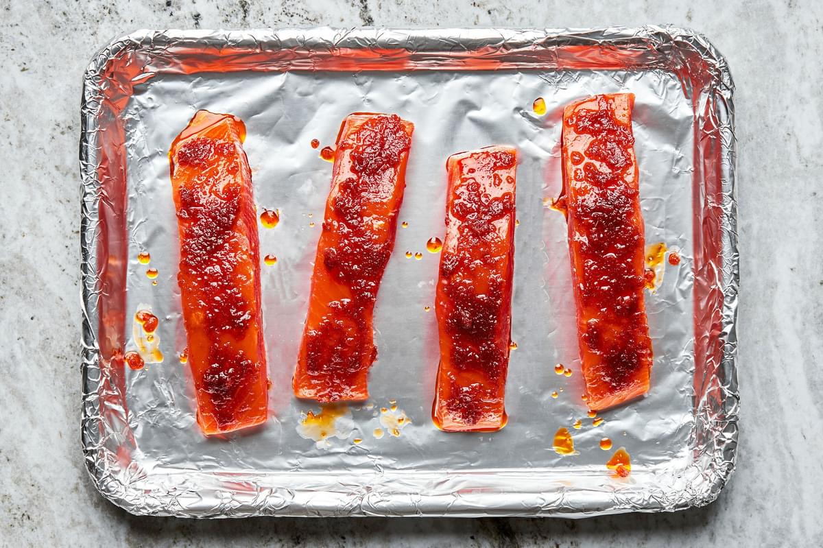 Four raw salmon filets seasoned with curry paste, salt, brown sugar and garlic power on a foil lined baking sheet