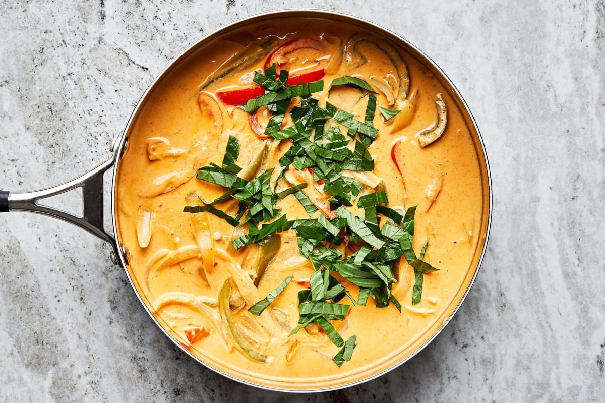 Coconut curry with bell peppers and fresh basil in a large skillet