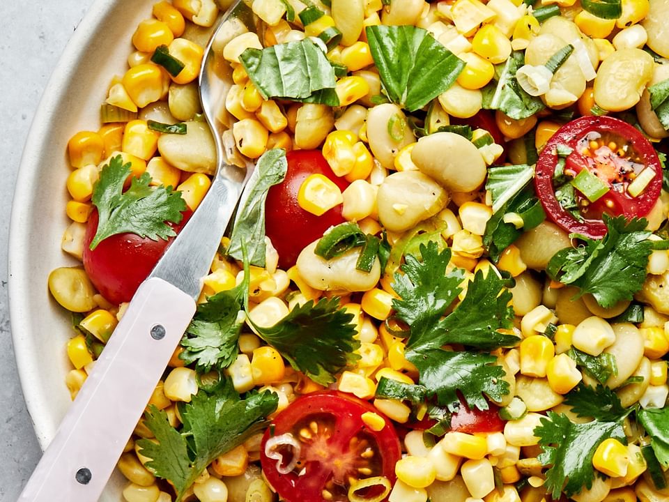 easy homemade succotash in a serving bowl with a spoon made with corn, lima beans, tomatoes, green onions, cilantro and basil