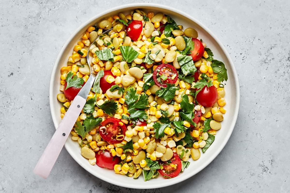 a bowl of easy succotash made with corn, lima beans, tomatoes, green onions, cilantro, basil, lime juice salt & pepper
