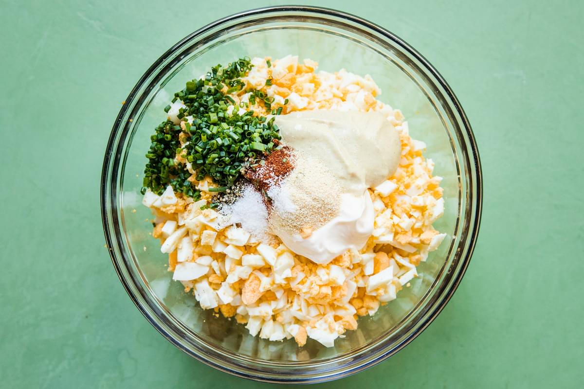 chopped boiled eggs, mayo, dijon, chives, apple cider vinegar and spices in a glass bowl to make an egg salad sandwich