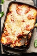 Eggplant parmesan in a black cast iron casserole with a large serving spoon scooping out a serving of eggplant parmesan