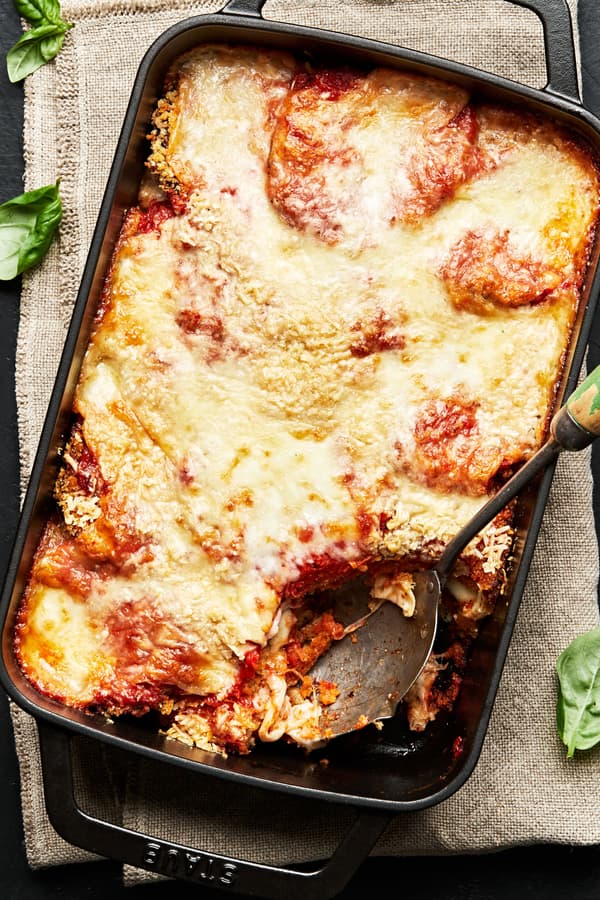 Eggplant parmesan in a black cast iron casserole with a large serving spoon scooping out a serving of eggplant parmesan