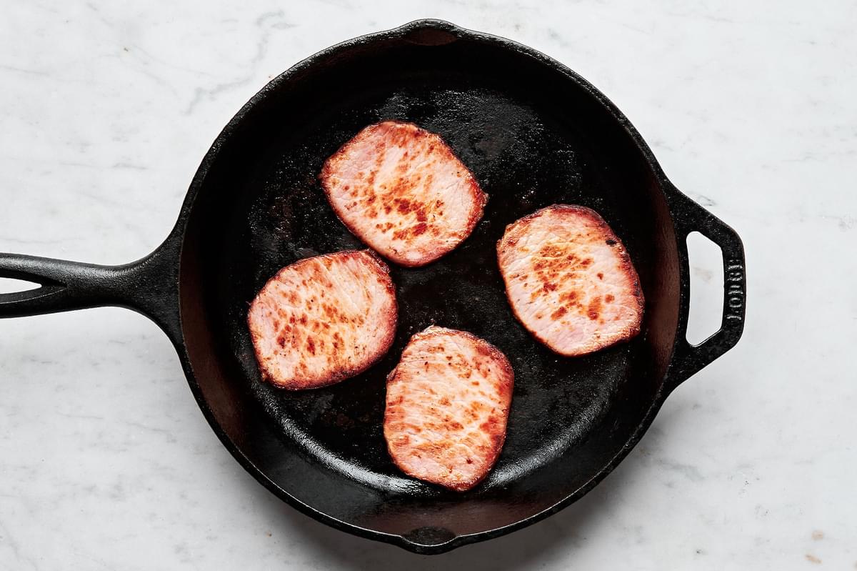 Canadian bacon being fried in a skillet