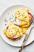 homemade eggs Benedict made with Canadian bacon and homemade hollandaise sauce on a plate with a fork