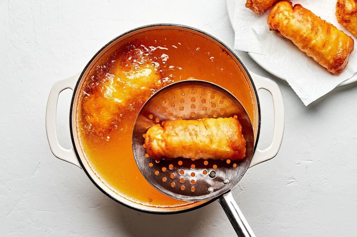 homemade beer battered cod being fried in a pot of oil and set on a paper lined plate to drain