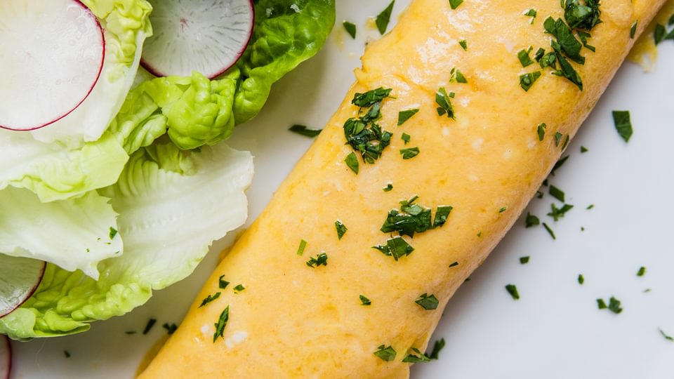 a homemade French omelette sprinkled with parsley on a plate next to a simple salad of crisp lettuce and thinly sliced radish