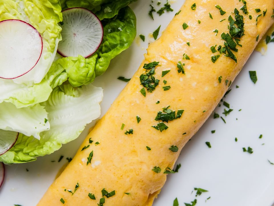 a homemade French omelette sprinkled with parsley on a plate next to a simple salad of crisp lettuce and thinly sliced radish