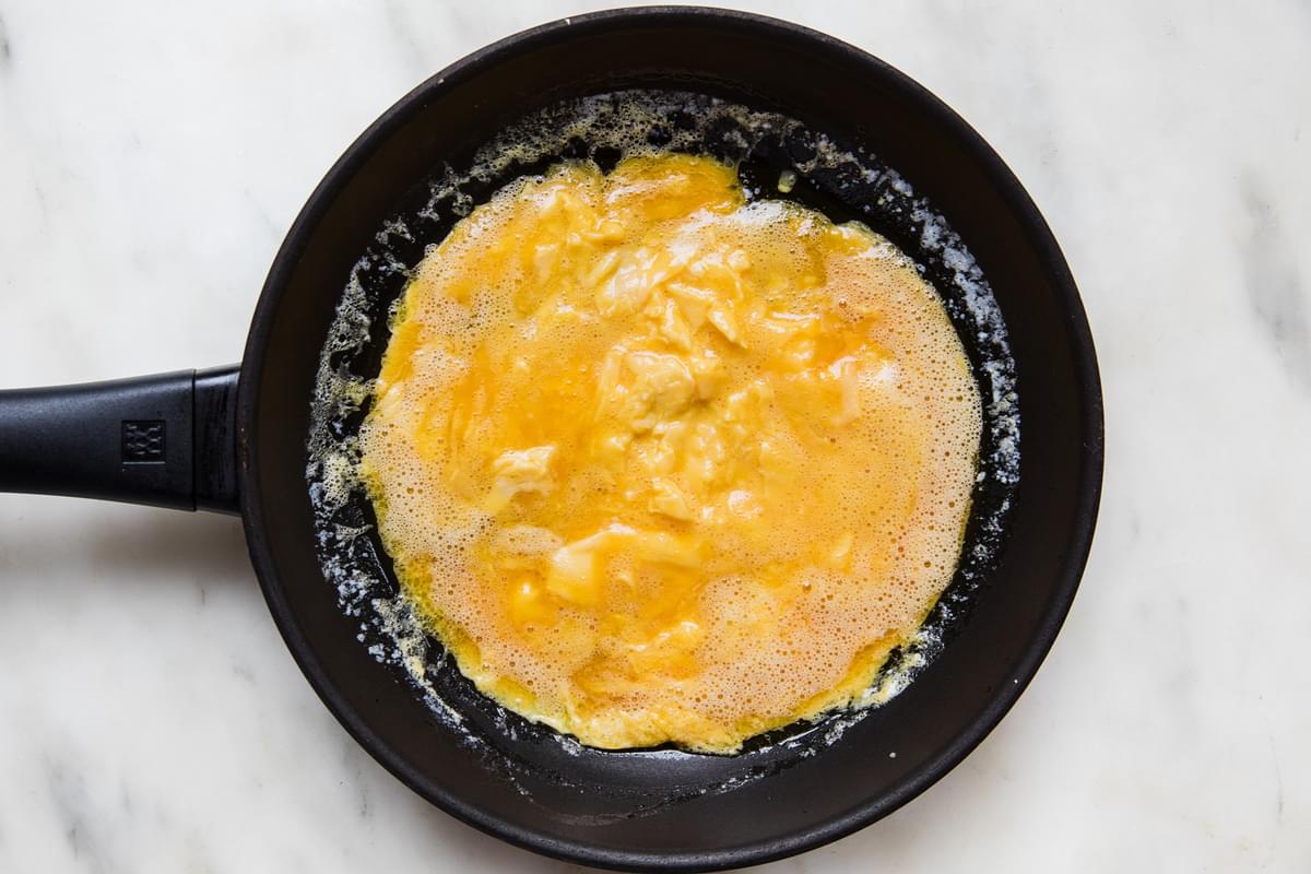 a non stick frying pan with melted butter and whisked eggs with salt poured in and set in an even layer for a French omelette